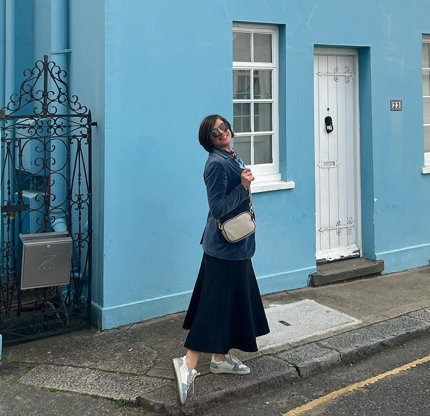 Image of Isida Mitre founder of Pashmisy outside a blue building. she is wearing one of Pashmisy's Italian silk scarves and smiling at the camera.